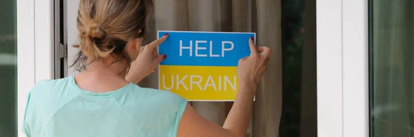 Woman sticking sign on door help Ukraine closeup. Charitable assistance for Ukrainian people concept