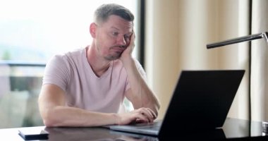 Boring man and stupid work man looks at laptop. Silly business tasks freelancer looking at laptop with dumb emotions sitting at table