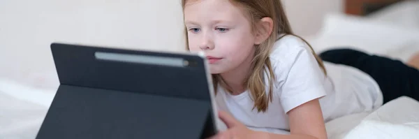 Kleines Mädchen Schaut Vorsichtig Auf Tablet Während Bett Liegt Mobile — Stockfoto