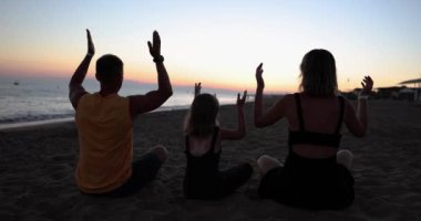 Aile plajda yoga yapıyor ve yaz tatilinde seyahat ediyor. Dinlenme ve aile uyumu.