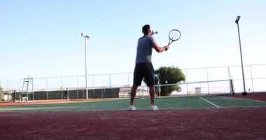 Kendine güvenen genç tenisçi raket ve top tutuyor ve sahaya vuruyor. Tenis oyunu ve tenis topu oyunda