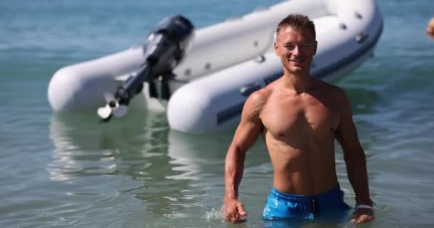英俊而微笑的运动员双手交叉地站在大海里 可充气汽艇和海上救生员 — 图库视频影像