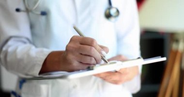 Hasta bilgilerini yazan kadın doktor pratisyen. Kardiyolog kağıt not defterine reçete yazıyor ve klinikte tıbbi belgelerle çalışıyor.
