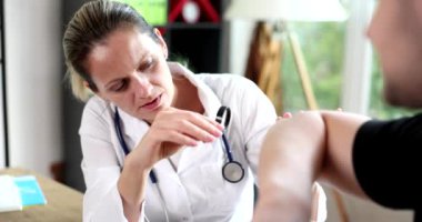 Doktor dermatolog, klinikte hastanın dirseğini büyüteçle muayene ediyor. Sedef hastalığı teşhisi, derinin soyulması ve kaşınması.