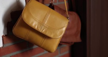 Sarı ve kahverengi deri çantalar duvara asılı duruyor. Moda çantası.