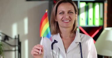Gülümseyen kadın doktor klinik 4K filminde ağır çekimde Igbt bayrağı sallıyor. lgbt topluluk konsepti için tıpta güçlendirme 