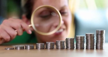 Büyüteç kullanan bir iş kadını yükselen para yığınlarını inceliyor. Finansal kar ve nakit geliri artışı