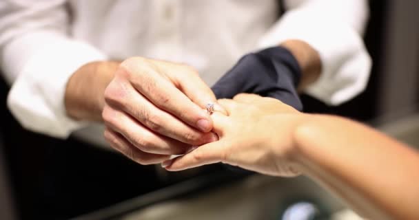 手袋の宝石商は女性の指に美しいダイヤモンドの婚約指輪を置きます ジュエリーフィッティング — ストック動画