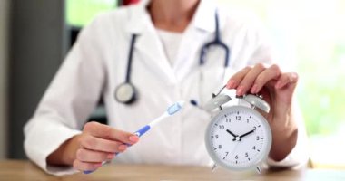 Diş hekimi diş fırçası ve çalar saati ağız temizliği sırasında elinde tutuyor. Diş hekiminde çalışan bir dişçi.