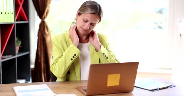 疲れた女はコンピューターで働くのに疲れた硬い首の痛み緊張した筋肉をマッサージ 間違った姿勢のビジネス女性は関節痛と腰痛を感じます — ストック動画