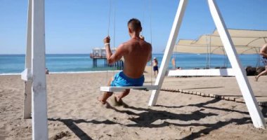 Sahilde, bir sporcu salıncağa biner, yakın plan, arka görüş. Deniz kıyısındaki eğlence anlayışı