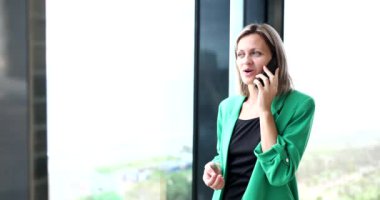 Ofiste pencerenin yanında duran bir kadın telefonla konuşuyor, yakın plan. İş yerinde mutluluk, çalışan.