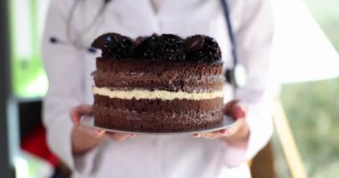Doktor büyük bir çikolatalı pasta tutuyor, yakın plan. Düşük karbonlu tatlı, sucrotor. Tıpta tatil