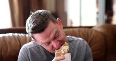 Kanepede mutlu bir adam shawarma yiyor, yakın plan. Eve fast food, Arap mutfağı.