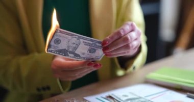 Ofiste oturan bir kadın dolar yakıyor, yakın plan, yavaş çekim. Sahte faturalar, para arzının azaltılması.