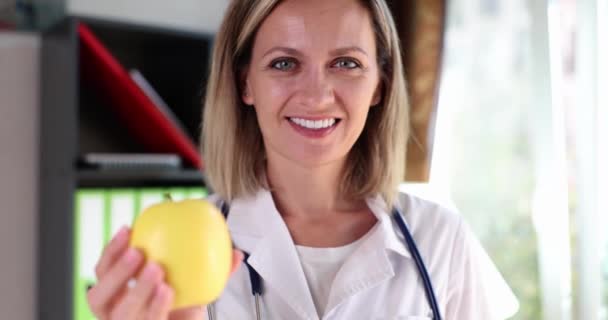 一个微笑的女人 一个诊所里的医生拿着一个黄色的苹果 一个特写 去看营养学家 适当营养 — 图库视频影像
