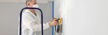 Portrait of male worker in protective costume polish wall with special equipment. Sander machine in work. Renovation, construction, interior design concept