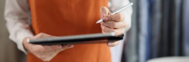 Close-up of dry cleaning company worker in uniform, girl hold tablet device with pen, high quality service, washing clothing. Dry cleaning, laundry concept