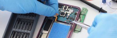 Close-up of technician fixing broken mobile phone, set new battery and cover, return old cellphone to life. Workplace with instruments. Handyman concept