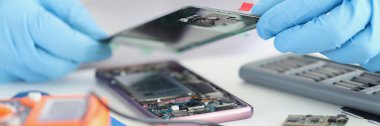Tamirci, bozuk akıllı telefonu tamir ederken, üstünü örterken, eldiven giyerken. Teçhizatla dolu bir işyeri. Tamir servisi, tamir, kullanışlı konsept