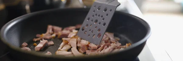 Close-up of chef stir ham or bacon slices on hot pan, person frying meat for breakfast or dinner. Cooking homemade food at home. Cooking, recipe concept