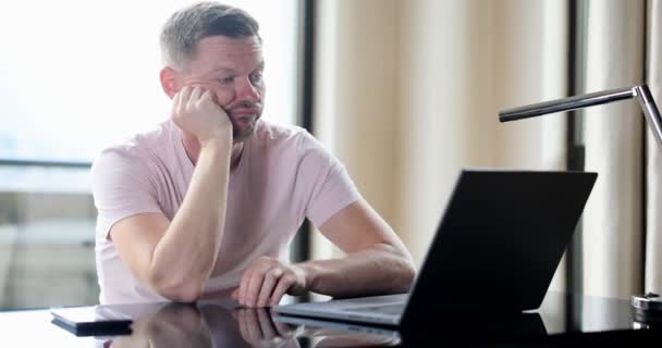 无聊的男人坐在家里的桌子上查看在线笔记本电脑内容 期待和失望的紧张情绪 — 图库视频影像