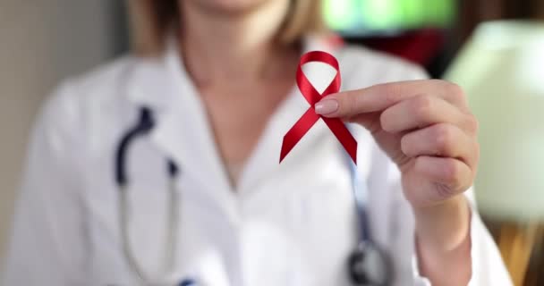 医師はエイズやHivから人々を守るための国際デーの赤いリボンのシンボルを手に持っています 獲得免疫不全症候群の発症による免疫系への損傷 — ストック動画