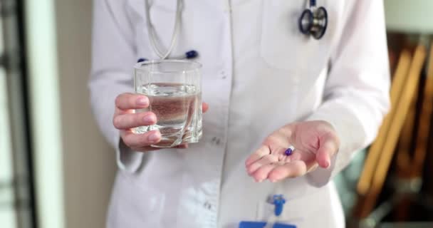 Χέρια Του Γιατρού Δίνουν Μπλε Άσπρο Χάπι Και Ένα Ποτήρι — Αρχείο Βίντεο