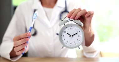 Klinikte çalışan dişçi doktorun elinde çalar saat ve diş fırçası var. Ağız temizliği zamanı.