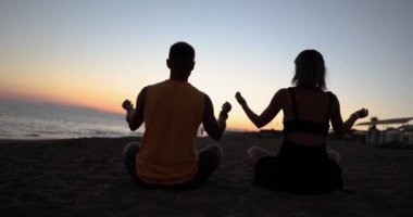 Çift gün batımında lotus pozisyonunda deniz kıyısında oturur. Yoga gevşeme ve rahatlama pratiği yapıyorum.