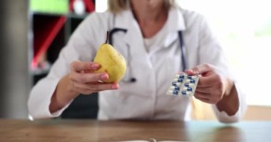 Doktor diyetisyen, ilaçların yakın planında sarı armut tutuyor. Vitamin ve meyve alımı kavramı