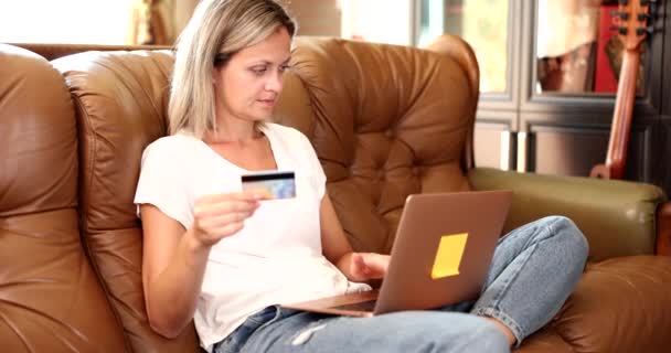 女人正坐在沙发上使用笔记本电脑和网上购物 网上购物的年轻女子快乐填写信用卡详情 — 图库视频影像