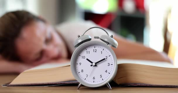 女の子は本と目覚まし時計でテーブルの上で寝る モチベーション怠惰学習と学生の疲労 — ストック動画