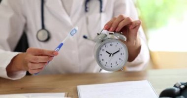 Doktor dişçi klinikte çalar saat ve diş fırçası gösteriyor. 4K film yavaş çekimde. Günlük diş fırçalama konsepti