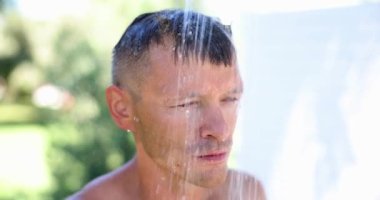 Yakışıklı adam yazın plajda duş alır. Sıcak bir gün ve serin bir duş.