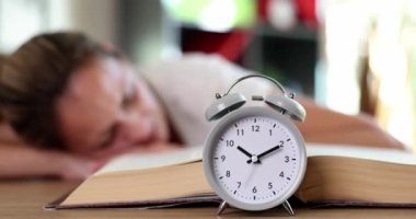 Açık kitaptaki kadının çalar saati yalan söyler ve masada uyur. Fazla çalışma, uykusuzluk ve aşırı çalışma