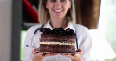 Gülümseyen doktor beslenme uzmanı çikolatalı pasta tutuyor. Şeker faydaları ve sağlık üzerindeki tatlı vücut etkilerine zarar