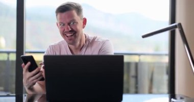 Adam masada oturuyor, akıllı telefondan ve laptoptan e-posta okuyor evet hareketi yapıyor ve mutlu oluyor. İşadamı büyük iş haberleri alıyor ve kariyer büyümesini kutluyor
