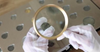 Nümismatist, büyüteçle bozuk para koleksiyonunu inceliyor. Antika paraların değeri