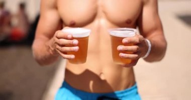 Sporty man on beach carries two glasses of beer. Cold beer and beach cafe