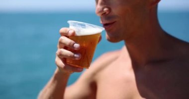 Man drinks beer on beach from plastic cup. Beach party and cold beer for tourists