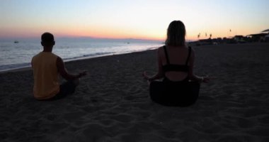 Silhouette of couple doing yoga at sunset on sea. Relax relaxation and lotus position
