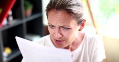 Portrait of woman who looks inquiringly and displeasedly at credit document. Woman with poor eyesight trying to read letter
