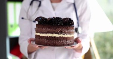 Doctor nutritionist holds in hand a high calorie chocolate cake. Doctor advises to give up unhealthy food