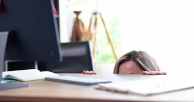 Shocked woman looks in fear from under table at monitor. Emotions of fear surprise shock and internet