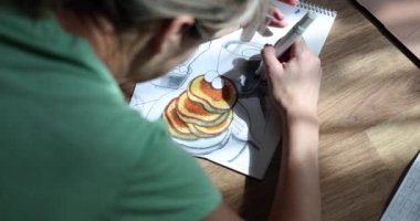 Woman draws in food album with pencil at home. Meditative drawing techniques concept