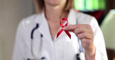 Red ribbon as symbol of fight against HIV in hands of doctor. World AIDS Day and medical care