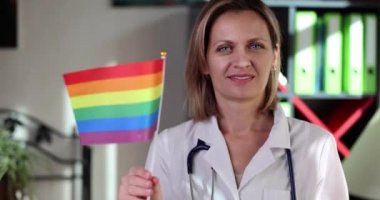 Smiling female doctor showing support for LGBTQ rainbow colored flag. Medicine healthcare support international symbol in pride month concept