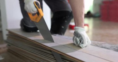 Worker cuts piece of laminate with hand saw closeup. Preparing laminate flooring for installation