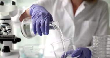 Scientist chemist pouring transparent liquid from flask into bottle closeup 4k movie slow motion. Drinking water quality control concept
